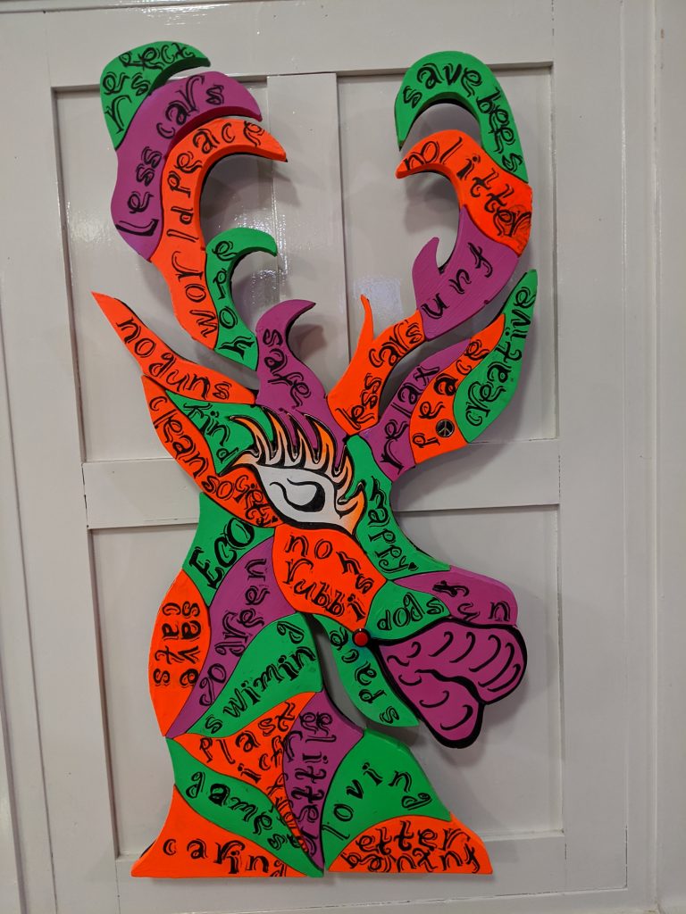 A cartoon style 'Reindeer' head in purple, orange and green with words printed on it.