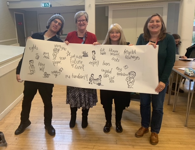 Image of four people holding up a sheet of paper with doodles and words on it.  In the centre it reads 'what is the future of care?'.
