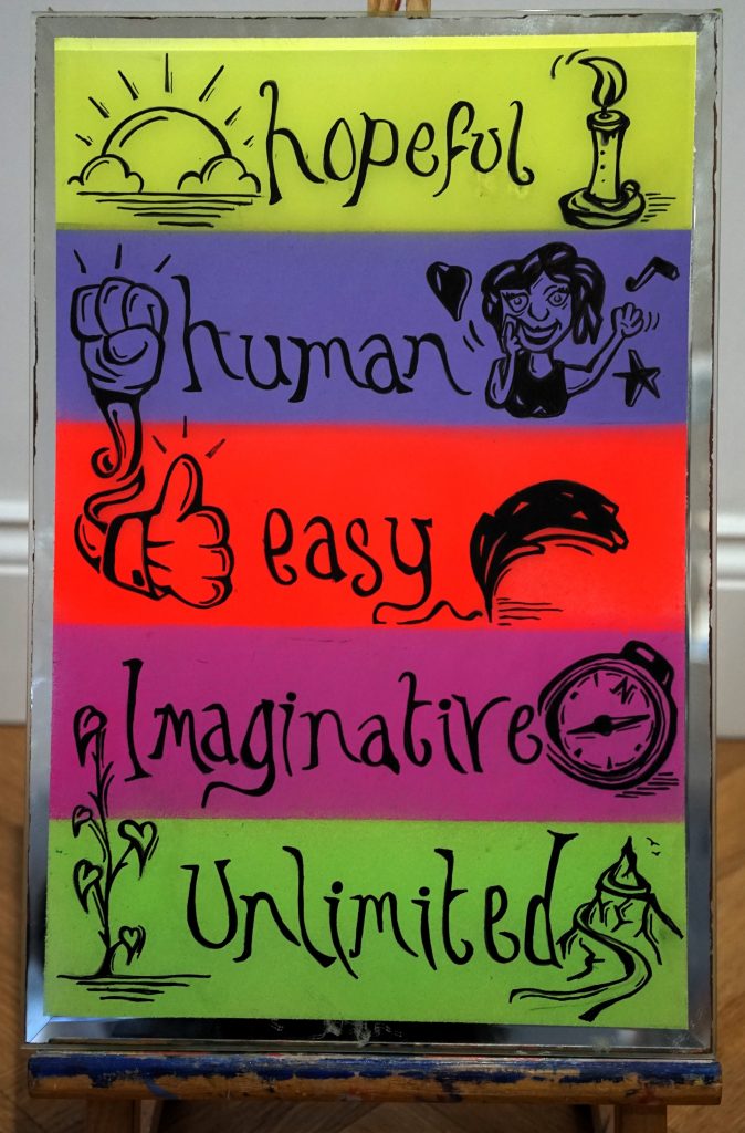 Image of a doodle on a mirror with five horizontal brightly coloured panels, it reads 'hopeful, human, easy, imaginative, unlimited'. 